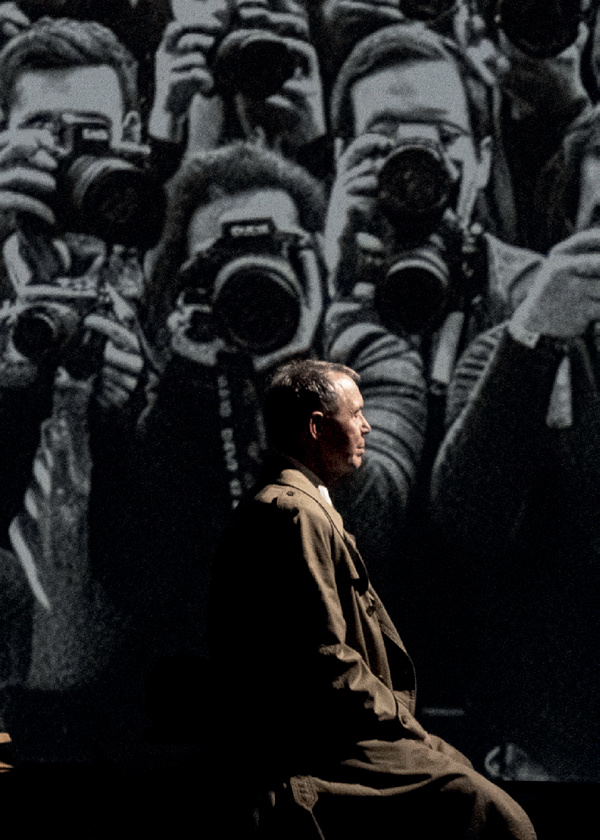 Acteur sur scène devant projection de photographes et public en silhouette