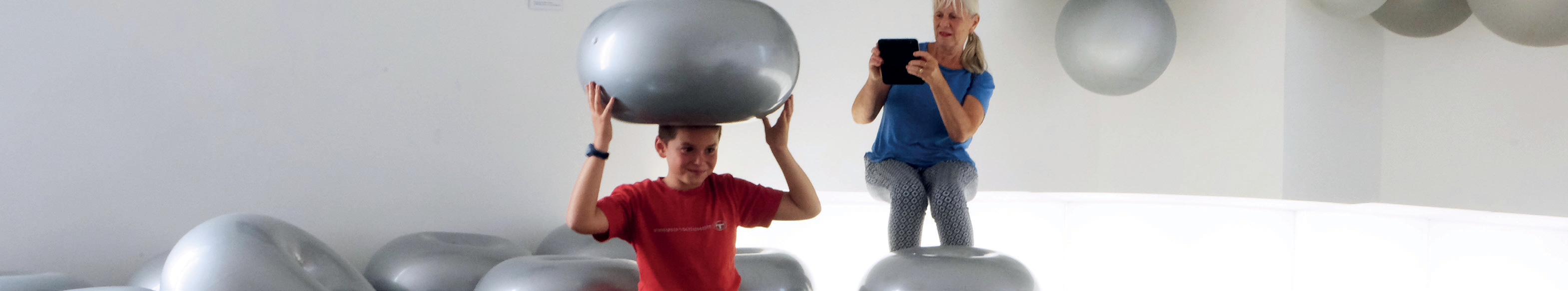 Enfant avec ballon argenté sur la tête, femme filmant à la tablette